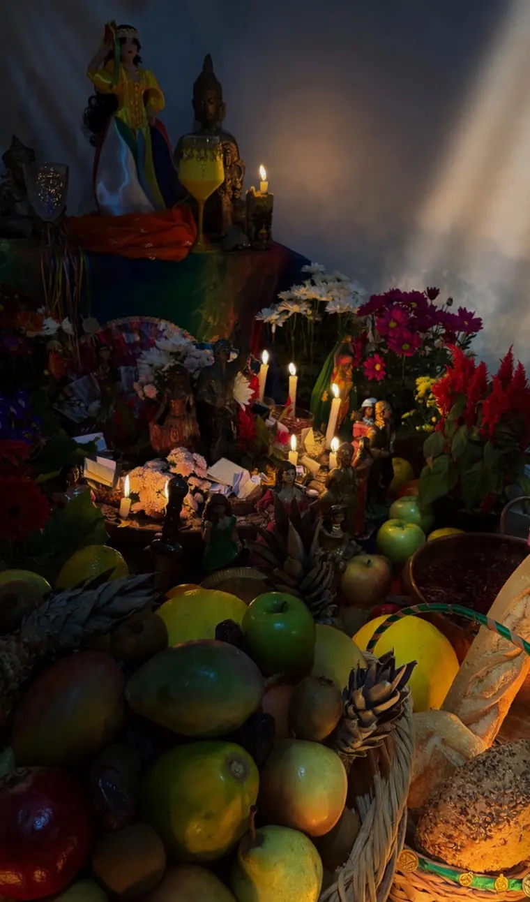 Altar com estátuas, velas acesas, flores e cestos de frutas e pães