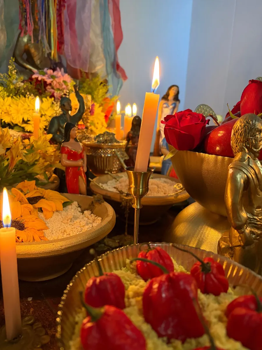 Altar com velas acesas, flores amarelas, rosas vermelhas e uma travessa com pimentas vermelhas