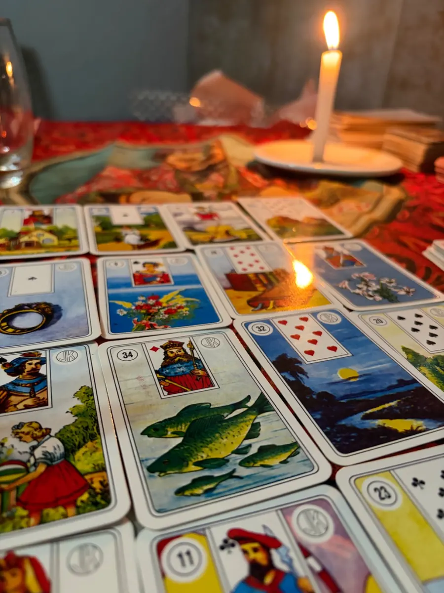 Baralho Cigano aberto sobre uma toalha vermelha, com uma vela acesa ao fundo