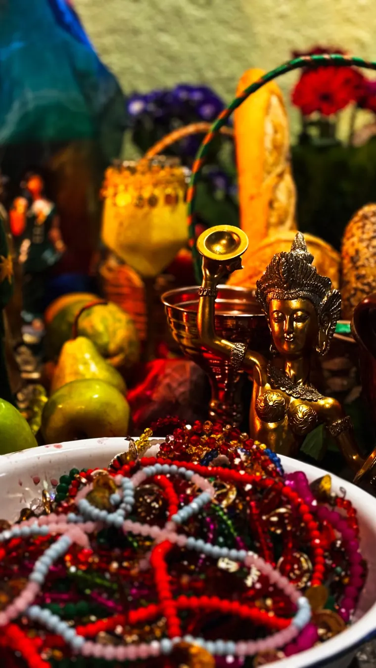 Estátua dourada ao lado de uma bacia com contas coloridas e frutas